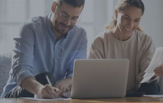 A couple sitting on a couch with a computer on a coffee table.