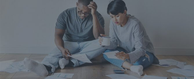 A couple sitting on a floor with papers scattered on the floor.