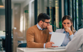 Portrait of a couple with financial problems looking at document in financial adviser's office.